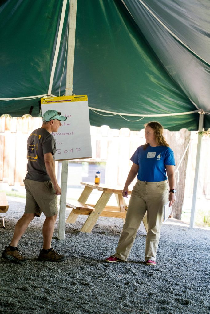 Two people standing by a whiteboard under a tent.