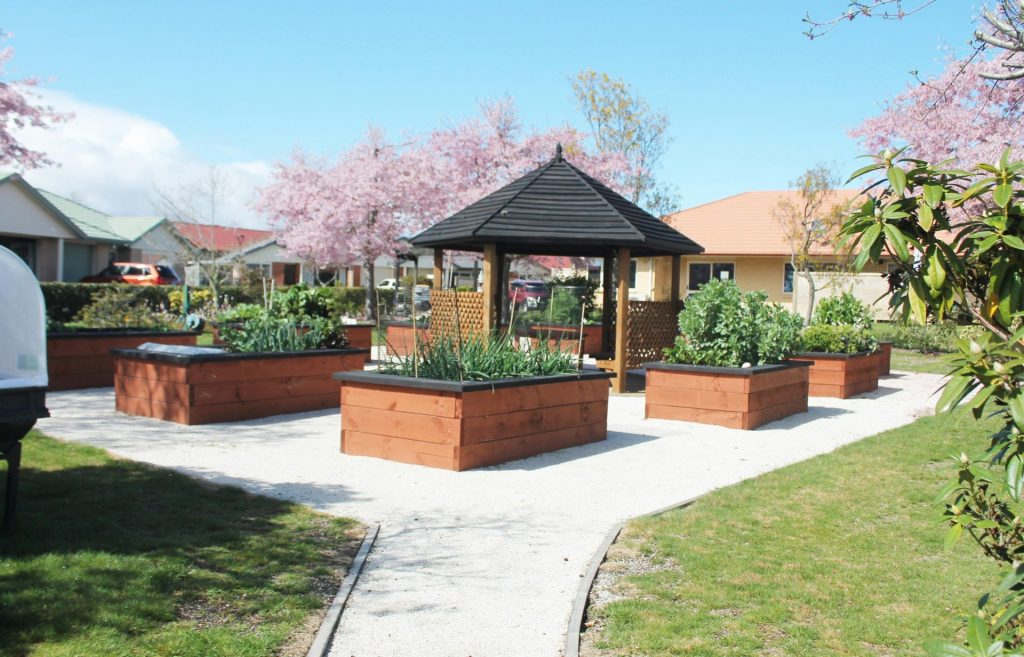 Raised garden beds surround a gazebo in a park.
